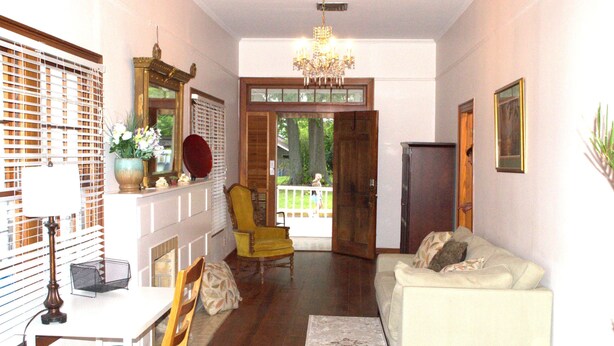 A living room with a sofa, a yellow armchair, a dining table with chairs, a chandelier, and a large window with blinds. - Walk to Downtown Scene (Lafayette)