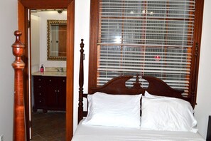 A bedroom with a wooden bed, a bathroom with a mirror and sink, and a window with blinds. - Walk to Downtown Scene (Lafayette)