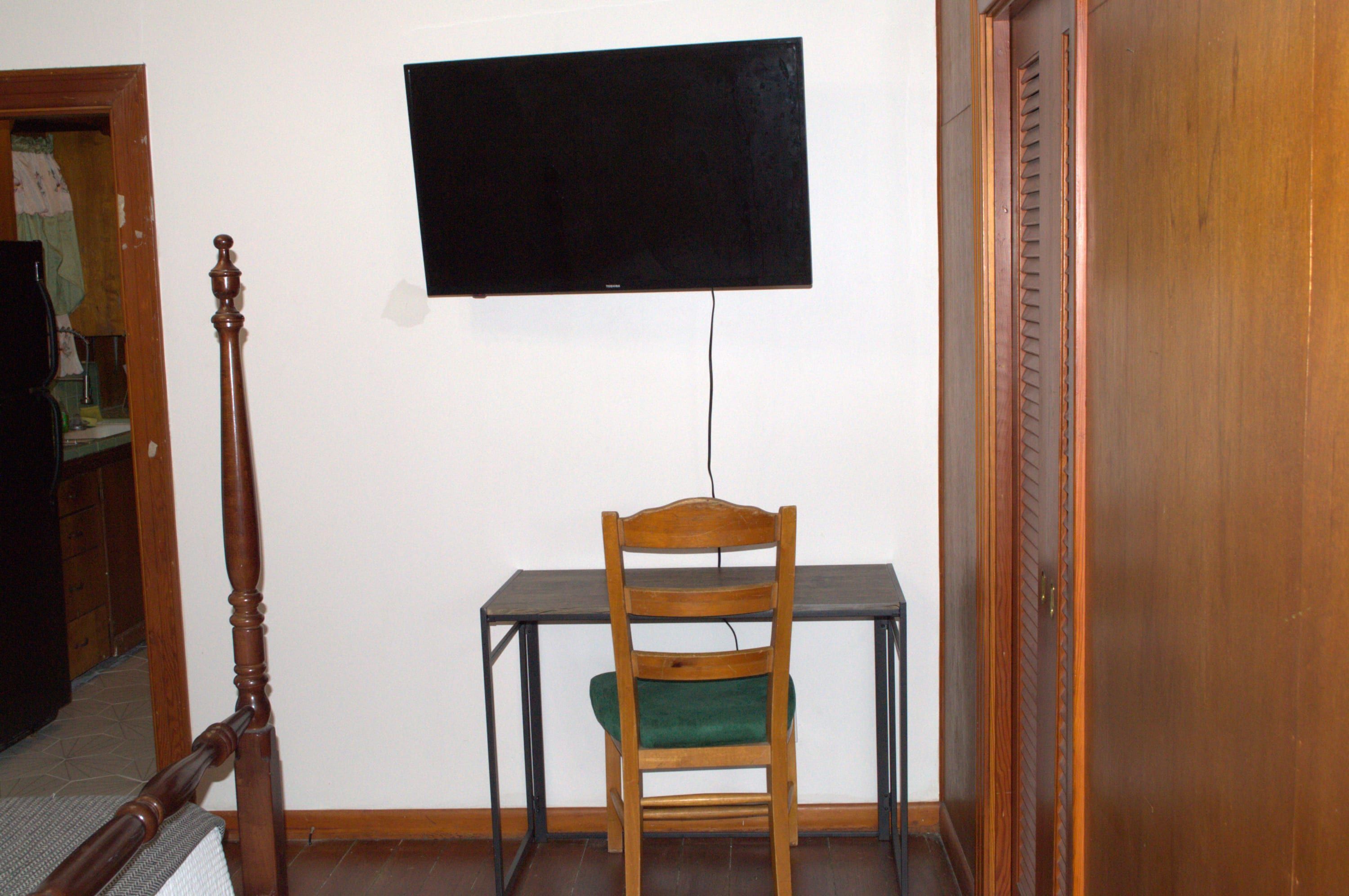 A room with a wooden chair, a small table, and a mounted television on the wall.