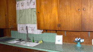 A kitchen with wooden cabinets, a green tiled backsplash, a sink, and a small table with cups. - Walk to Downtown Scene (Lafayette)