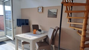 Un comedor con una mesa de madera, cuatro sillas, un reloj, un cuadro y una escalera de madera.