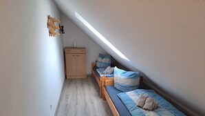 Una habitación pequeña y estrecha con techo inclinado, un armario de madera, una cama con ropa de cama azul y una mesita.