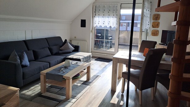 Una sala moderna con un sofá oscuro, una mesa de centro de madera y una zona de comedor con una mesa y sillas.