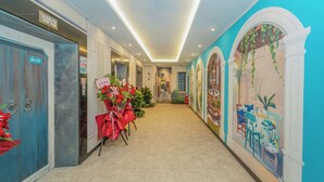 Un couloir d’hôtel avec un sol carrelé, une composition florale et une fresque sur le mur de droite.