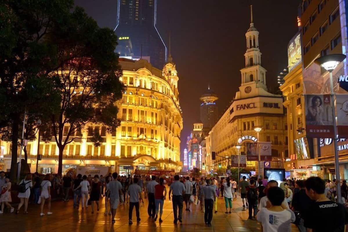 Una animada plaza urbana con edificios históricos, incluyendo una destacada torre del reloj y un edificio con la señalización 'FANCL'.