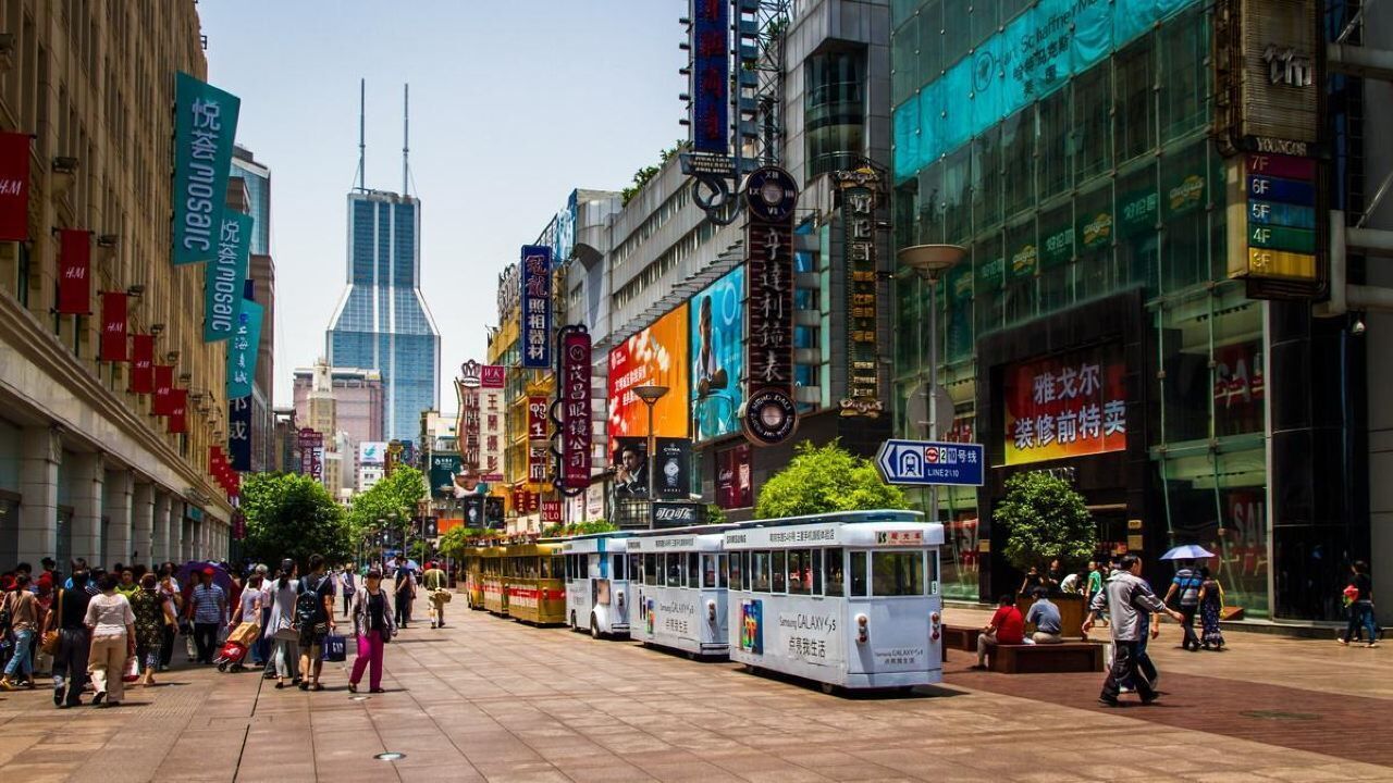 A bustling urban street with a tram line, pedestrians, and commercial buildings with various signs and advertisements.