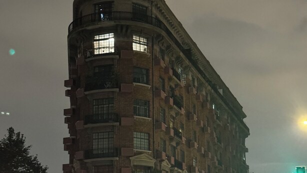 Un immeuble à plusieurs étages doté d’une façade incurvée, de grandes fenêtres et d’une entrée au niveau du sol, avec une porte et un petit auvent.