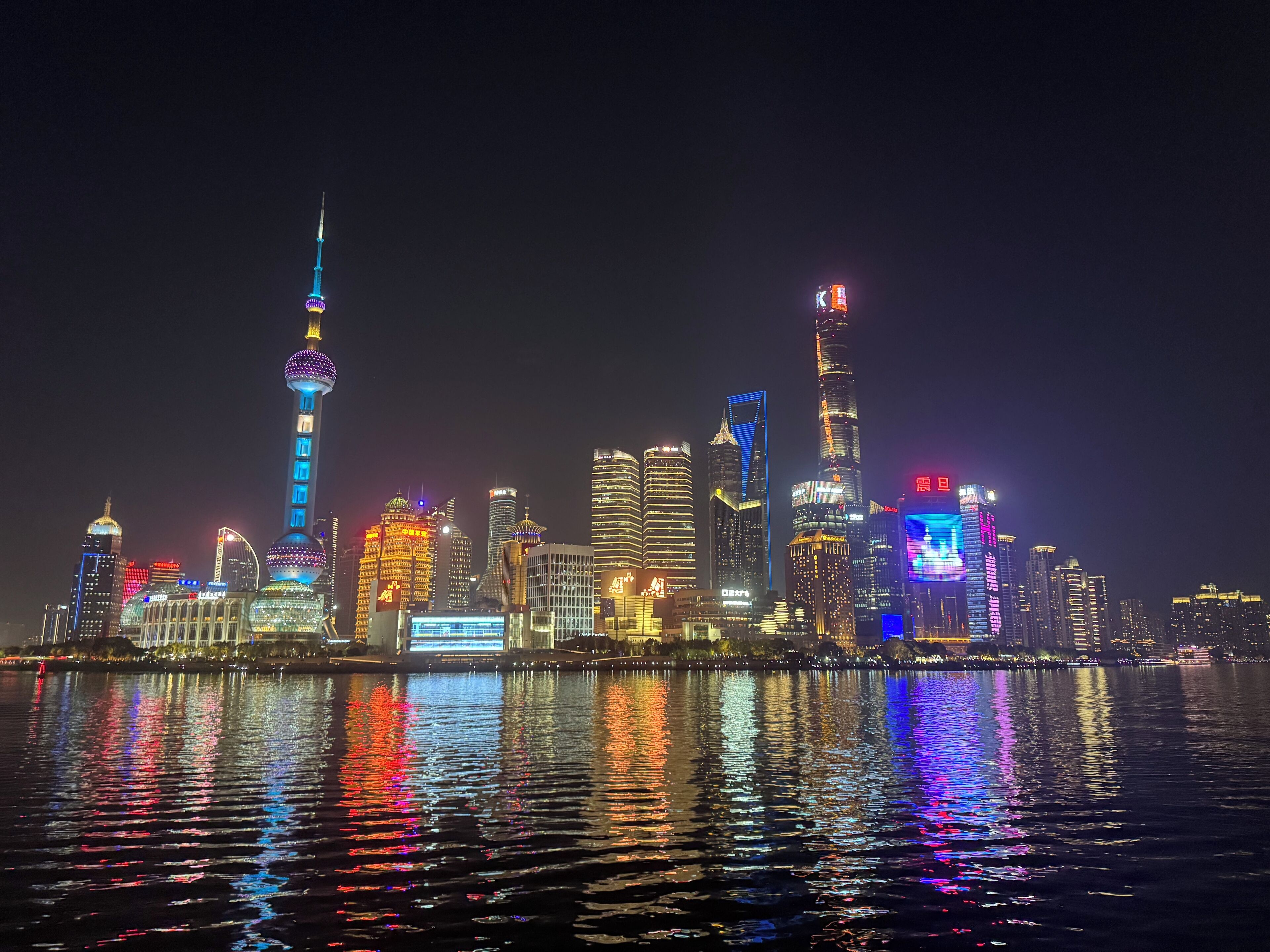 A nighttime city skyline with illuminated buildings reflecting on the water.