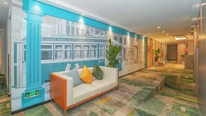 Un hall d’hôtel avec une grande fresque murale, un canapé avec des coussins et une moquette à motifs.