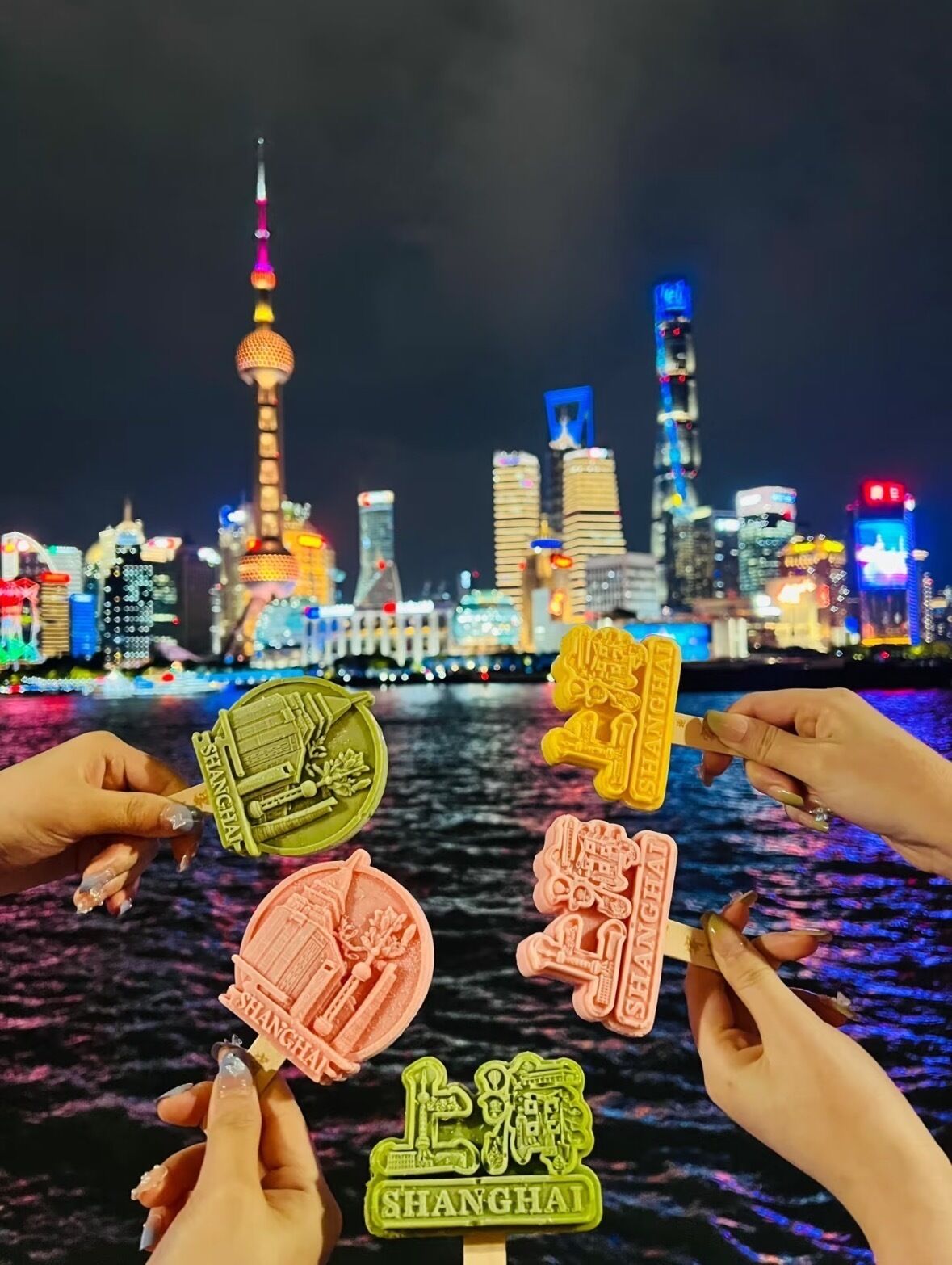 A night view of a city skyline with illuminated buildings and a river in the foreground.