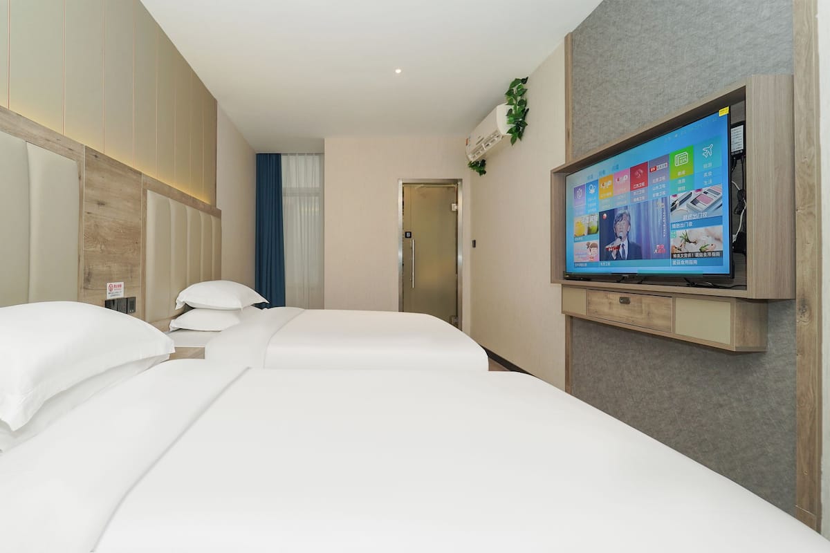 Una habitación de hotel con dos camas, un televisor montado en la pared y una puerta que da a otra habitación.