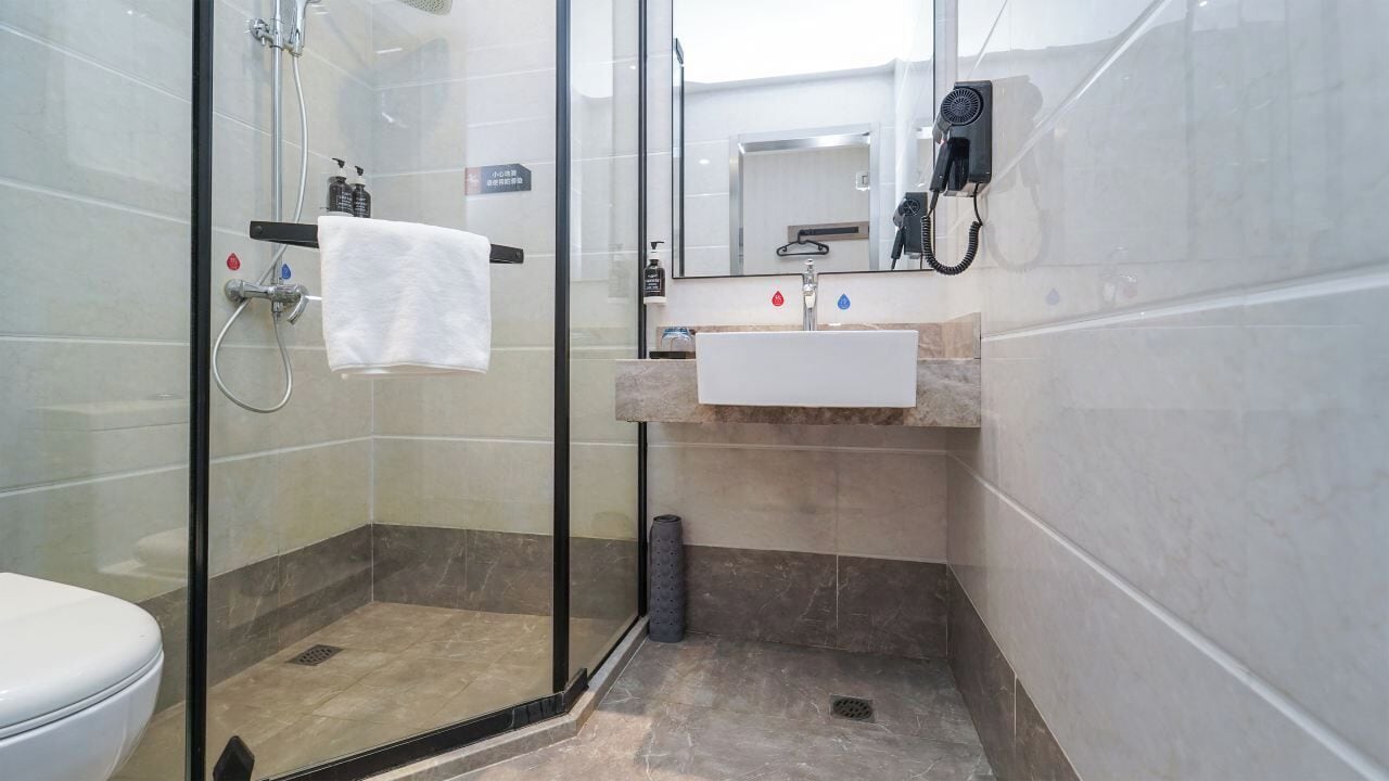 A modern bathroom with a glass shower enclosure, a white sink, and a handheld hair dryer.