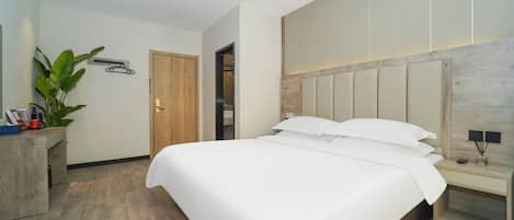 Une chambre d’hôtel moderne avec un grand lit, une tête de lit en bois, une table de chevet, un bureau et une plante en pot.