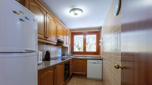 A kitchen with wooden cabinets, a white refrigerator, a dishwasher, and a window with a view of trees. - Andorra Stunning Views Apartment (El Tarter)