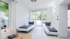 Ein modernes, minimalistisches Schlafzimmer mit zwei Einzelbetten, einem kleinen Tisch und einem großen Fenster mit Blick auf Grün.