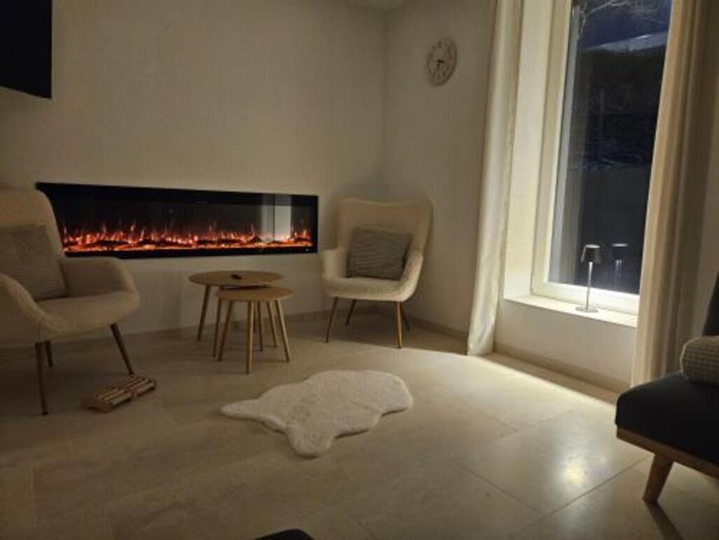 A living room with a fireplace, two armchairs, a round table, and a fur rug.