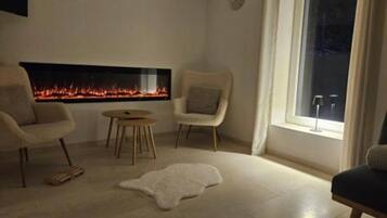 A living room with a fireplace, two armchairs, a round table, and a fur rug.