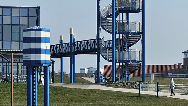 Un'area giochi con una struttura a scacchi blu e bianca, una scala a chiocciola e una torre con tetto verde.