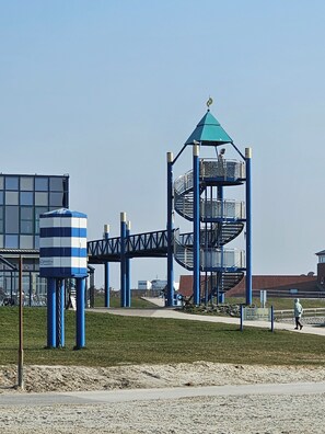Un terrain de jeux doté d’une structure à carreaux bleus et blancs, d’un escalier en colimaçon et d’une tour surmontée d’un toit végétalisé.