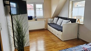 Una camera mansardata con un letto, un termosifone, una pianta e una TV fissata al muro.