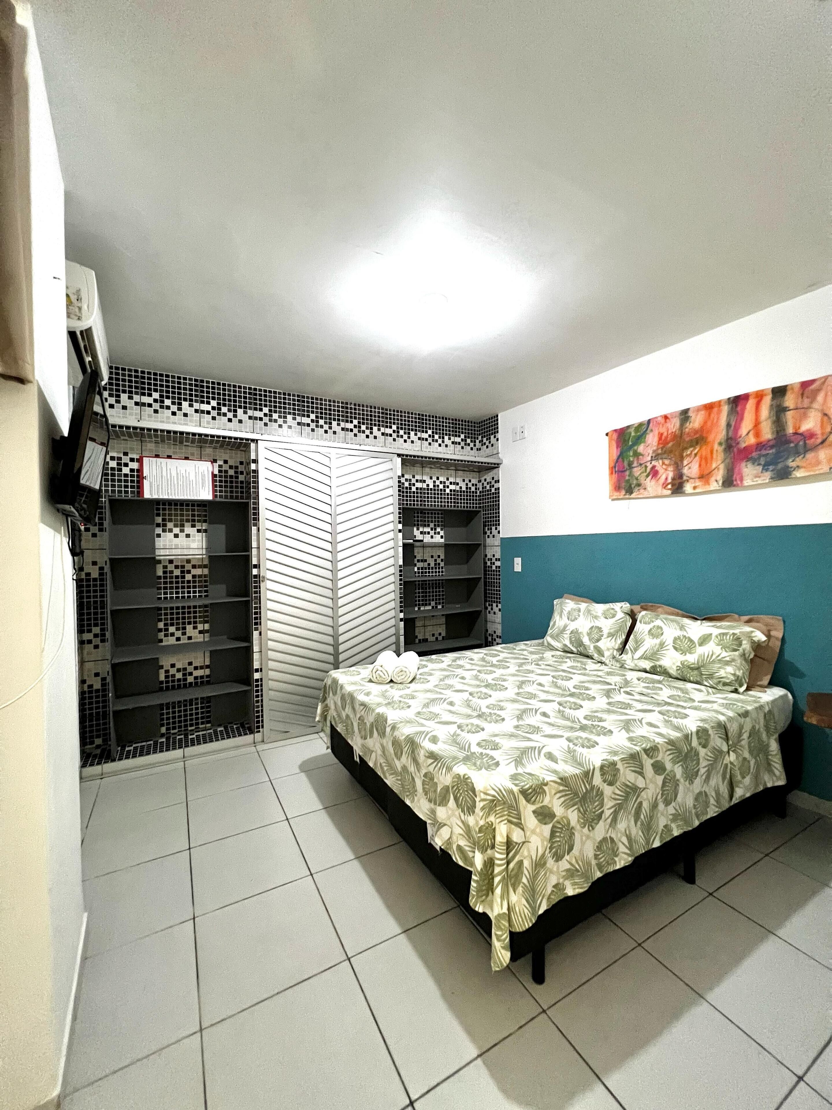 Un dormitorio con una cama, una estantería y un cuadro abstracto de colores en la pared.