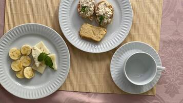 A table with two plates of food, one with sliced bananas and cheese, and the other with bread and a creamy spread. There's also a cup and saucer on the table.