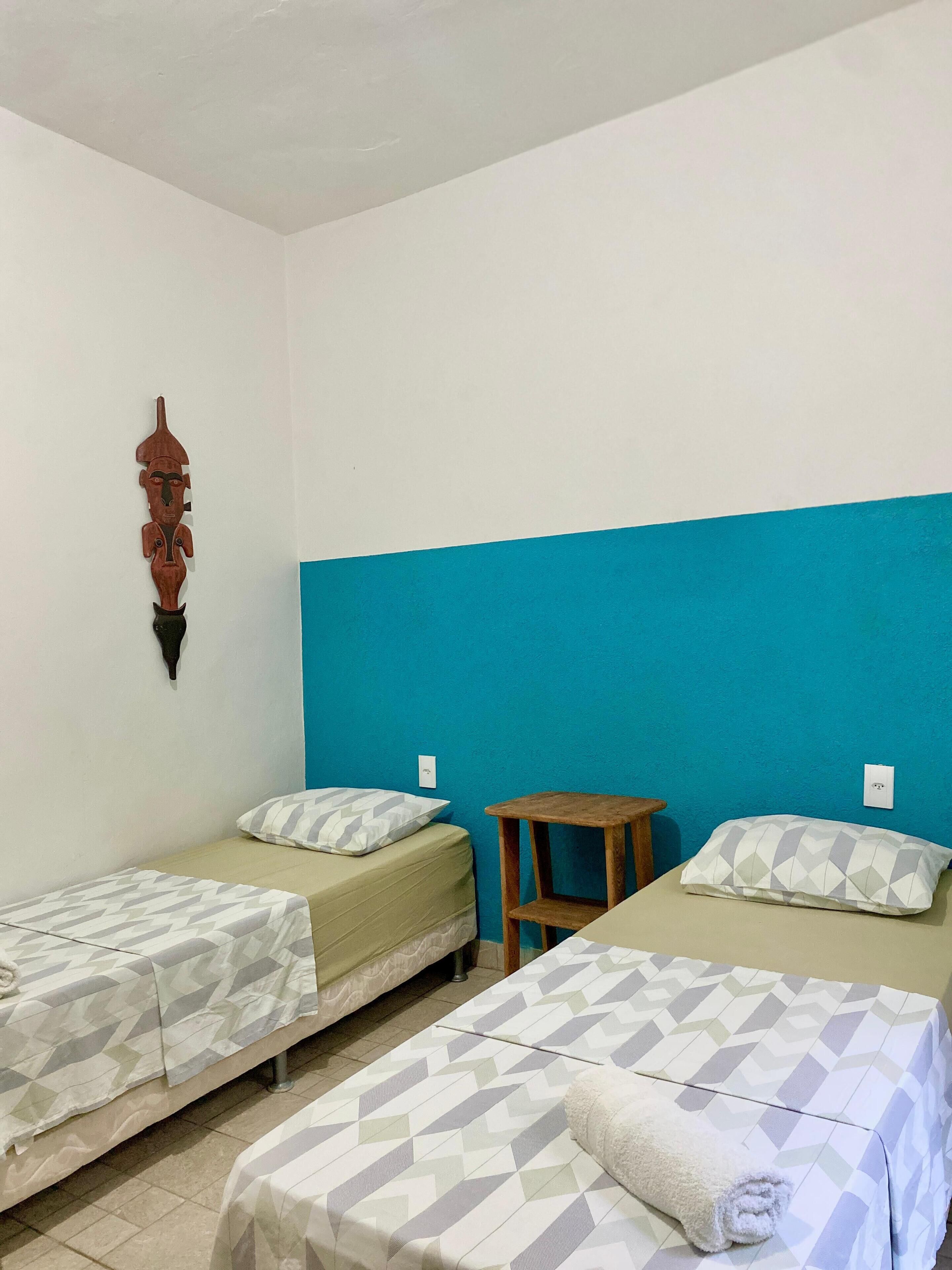 Een kamer met twee bedden, een klein houten krukje en een decoratief object aan de muur.