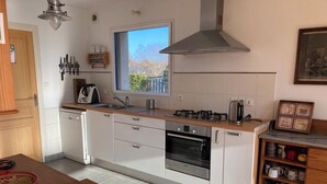 A modern kitchen with white cabinets, a stainless steel range hood, a window with a view, and a coffee-themed decoration. - Spacious and bright house on large plot 10 min walk from Pont L' Abbé (Pont-l'Abbé)