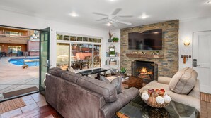 A modern living room with a fireplace, comfortable seating, and a view of a pool and outdoor area. - Fasching Haus 190 (Aspen)