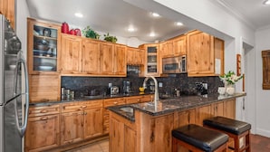 A kitchen with wooden cabinets, granite countertops, stainless steel appliances, and a central island with stools. - Fasching Haus 190 (Aspen)