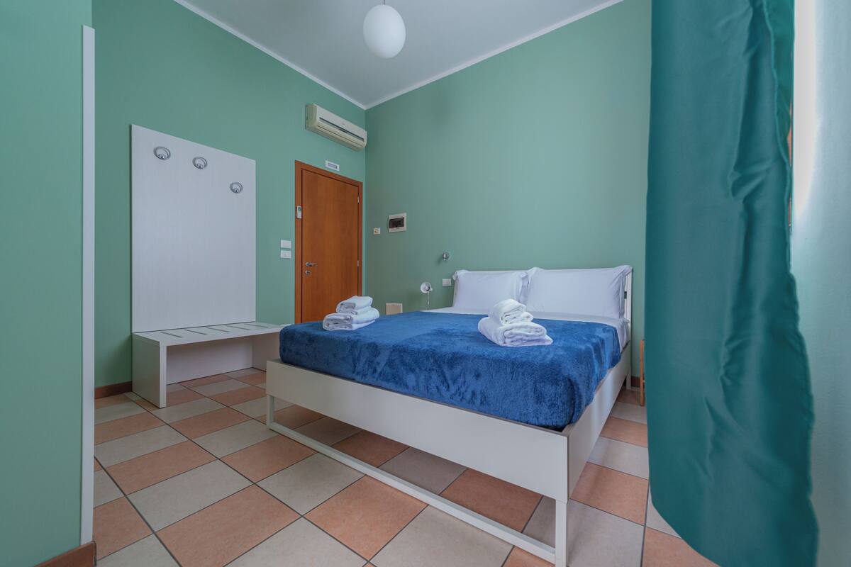 A bedroom with a bed, a wardrobe, a bench, and an air conditioning unit.