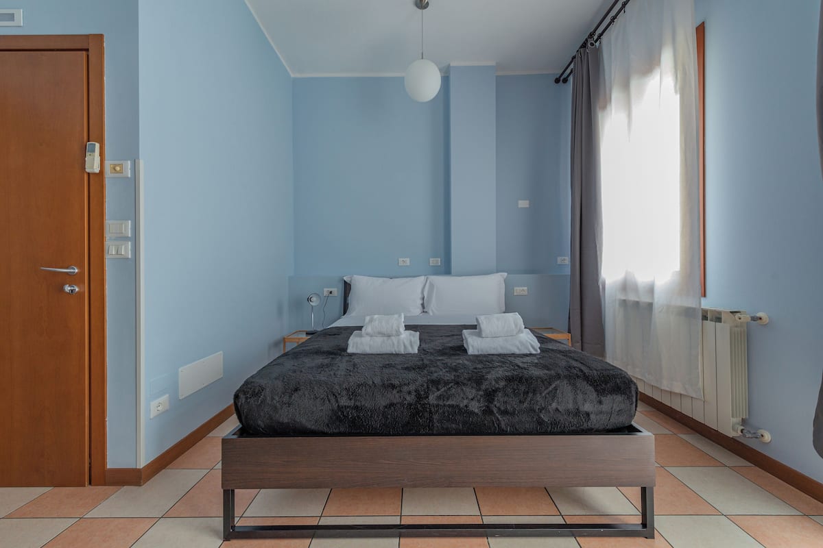 A bedroom with a bed, a wooden door, a light fixture, and a window with curtains.