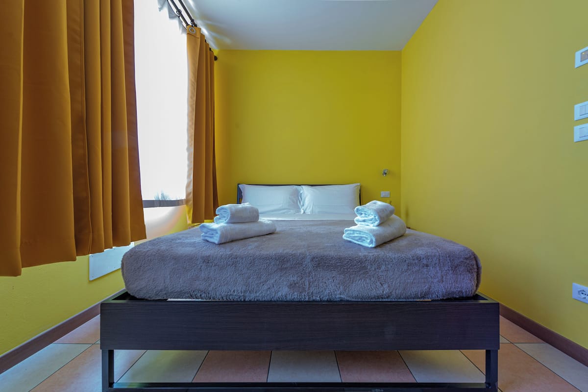 A bed with a white mattress and pillows, a dark wooden frame, and two folded towels on the bed.