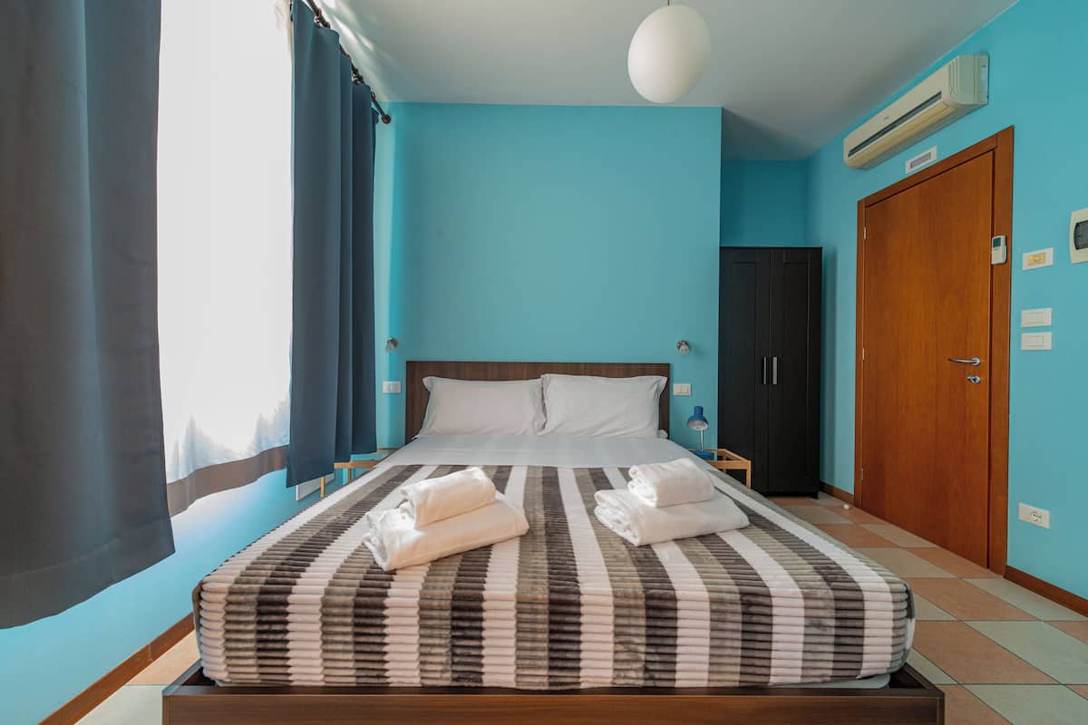 A hotel room with a large bed, a wooden wardrobe, a nightstand, and a wall-mounted air conditioner.