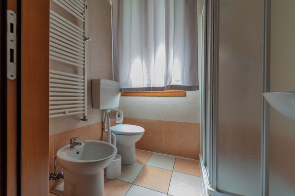 Un baño con lavamanos, inodoro y ventana con cortina.