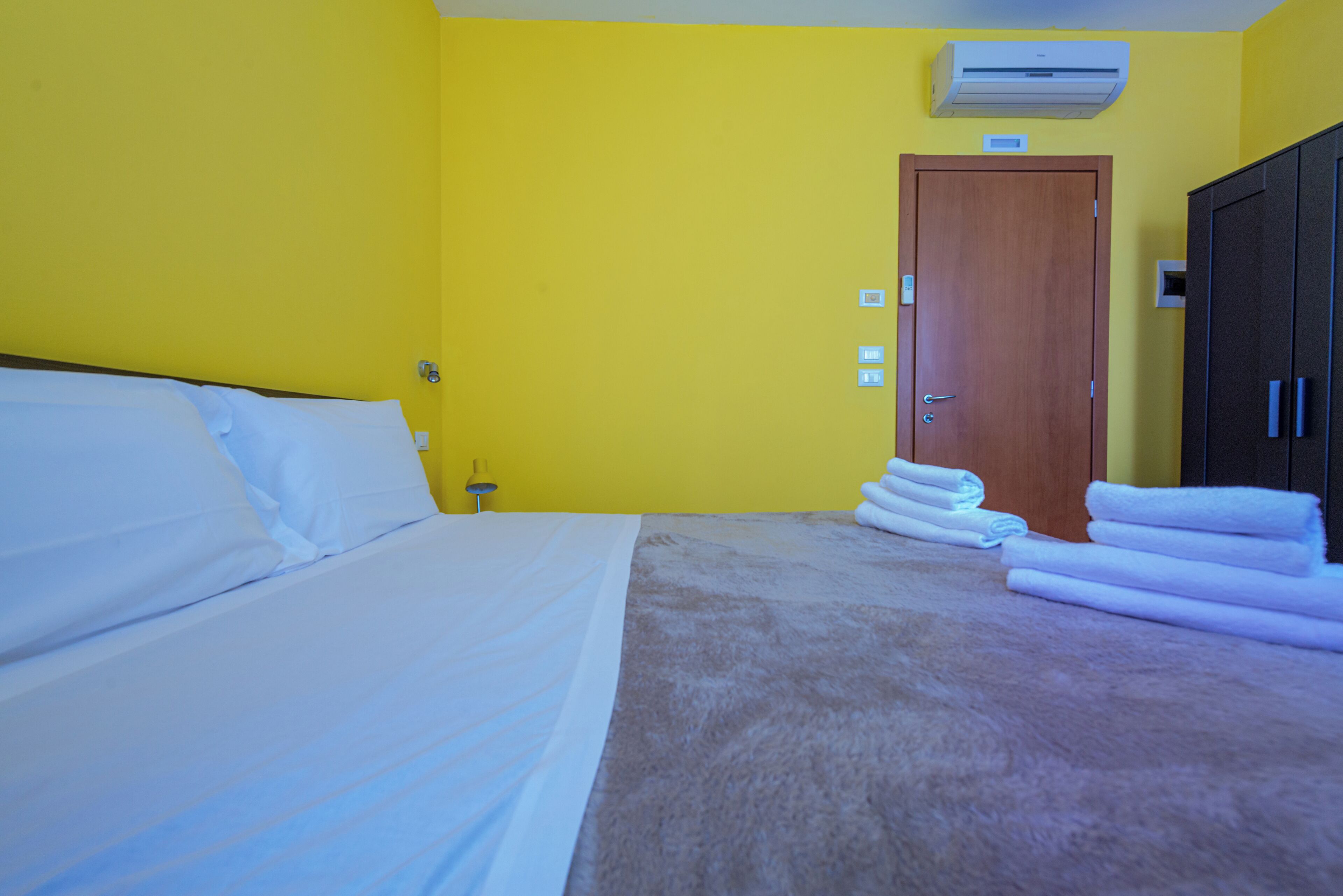 A hotel room with a bed, a wooden door, and a stack of towels.