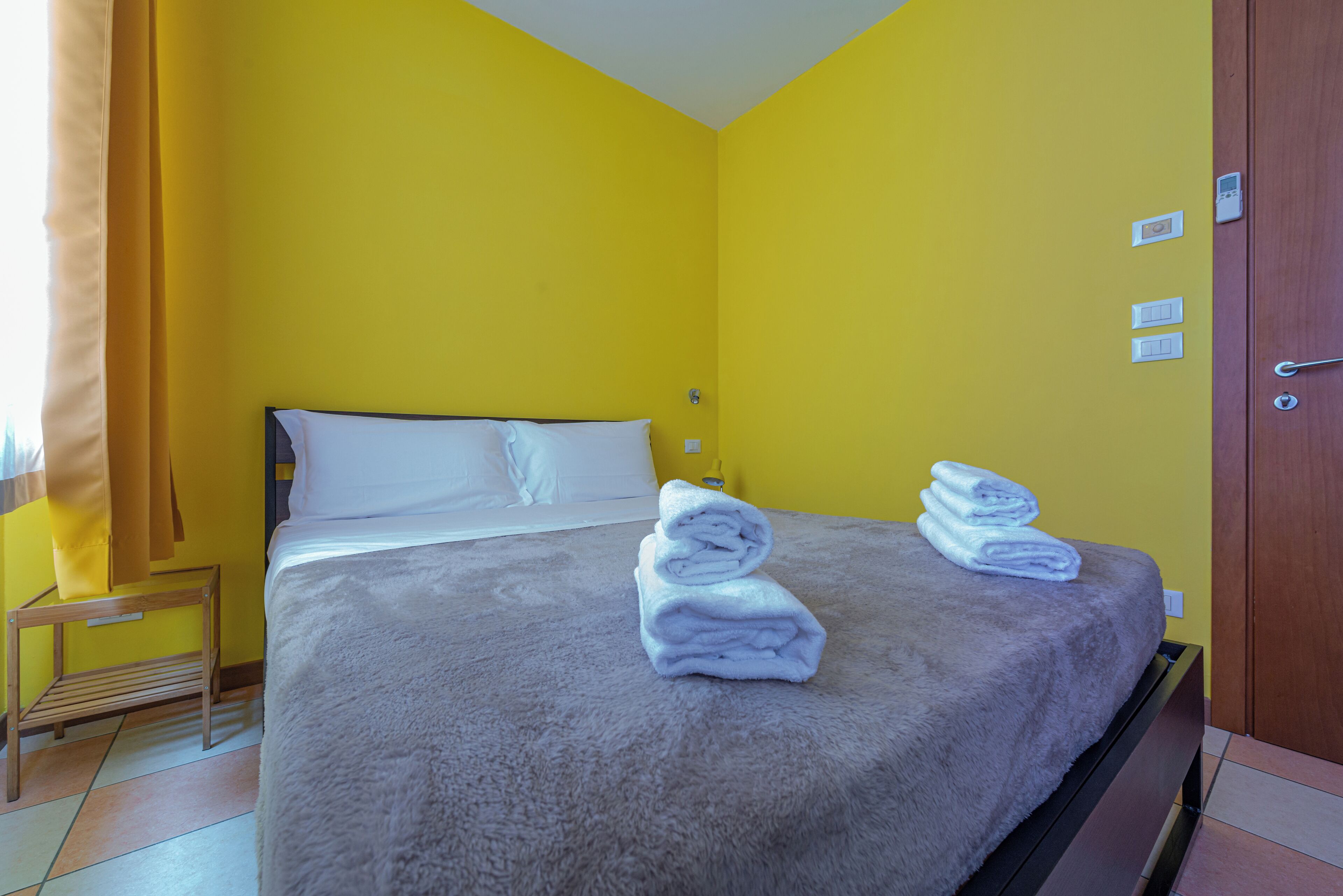Un dormitorio con una cama, dos toallas enrolladas, una mesita de noche y un buró.