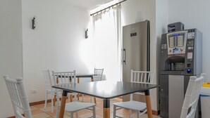 Een kleine keuken met een eettafel, stoelen, een koelkast en een koffieapparaat.