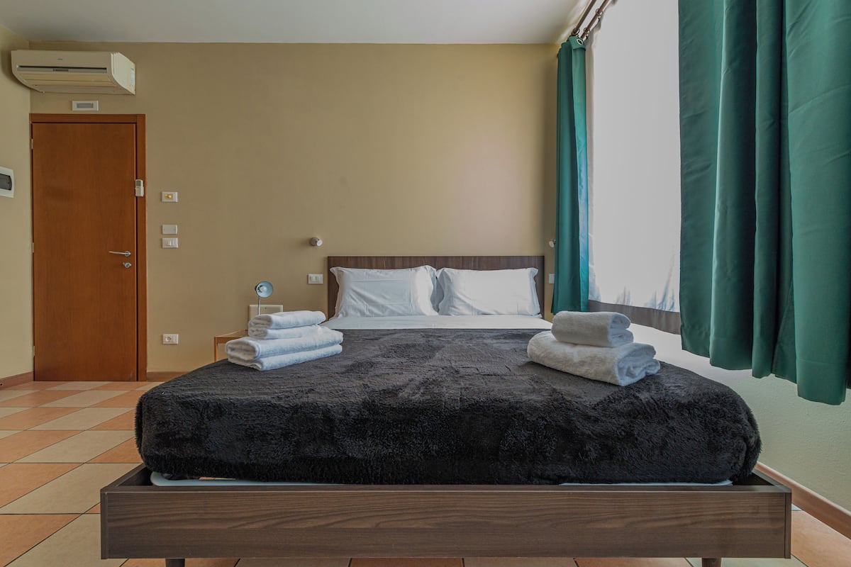 A bedroom with a large bed, a wooden headboard, and a window with curtains.