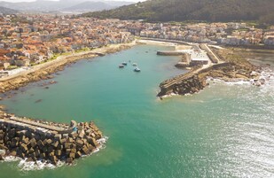 Vista aérea de un pueblo costero con un puerto, edificios y un rompeolas rocoso.