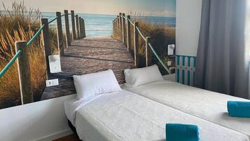 Habitación de hotel con cama, dos almohadas, una toalla azul y un mural de un muelle que conduce al mar.