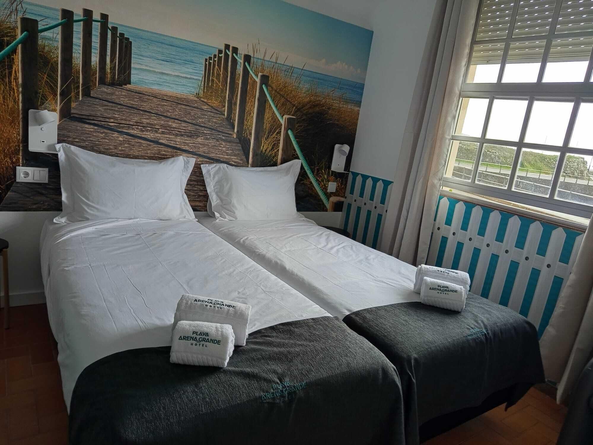 A double bed with white linens, two pillows, and two towels with the hotel name.