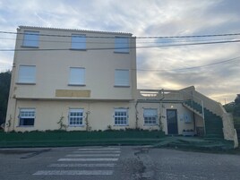 Un edificio de varios pisos con fachada plana, una escalera que conduce a la entrada y un paso de peatones enfrente.