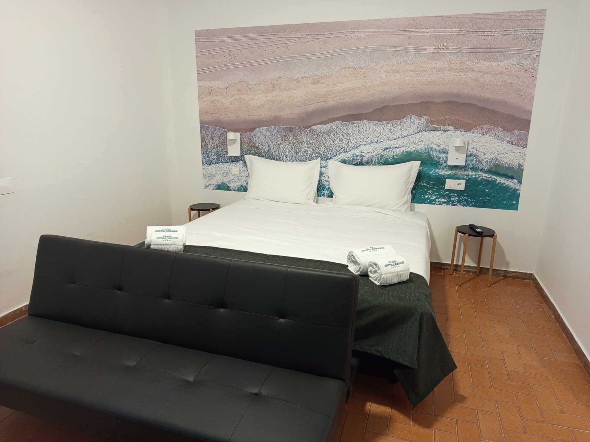 Une chambre d’hôtel avec un lit, un canapé noir, une grande fresque murale et deux tables de chevet.