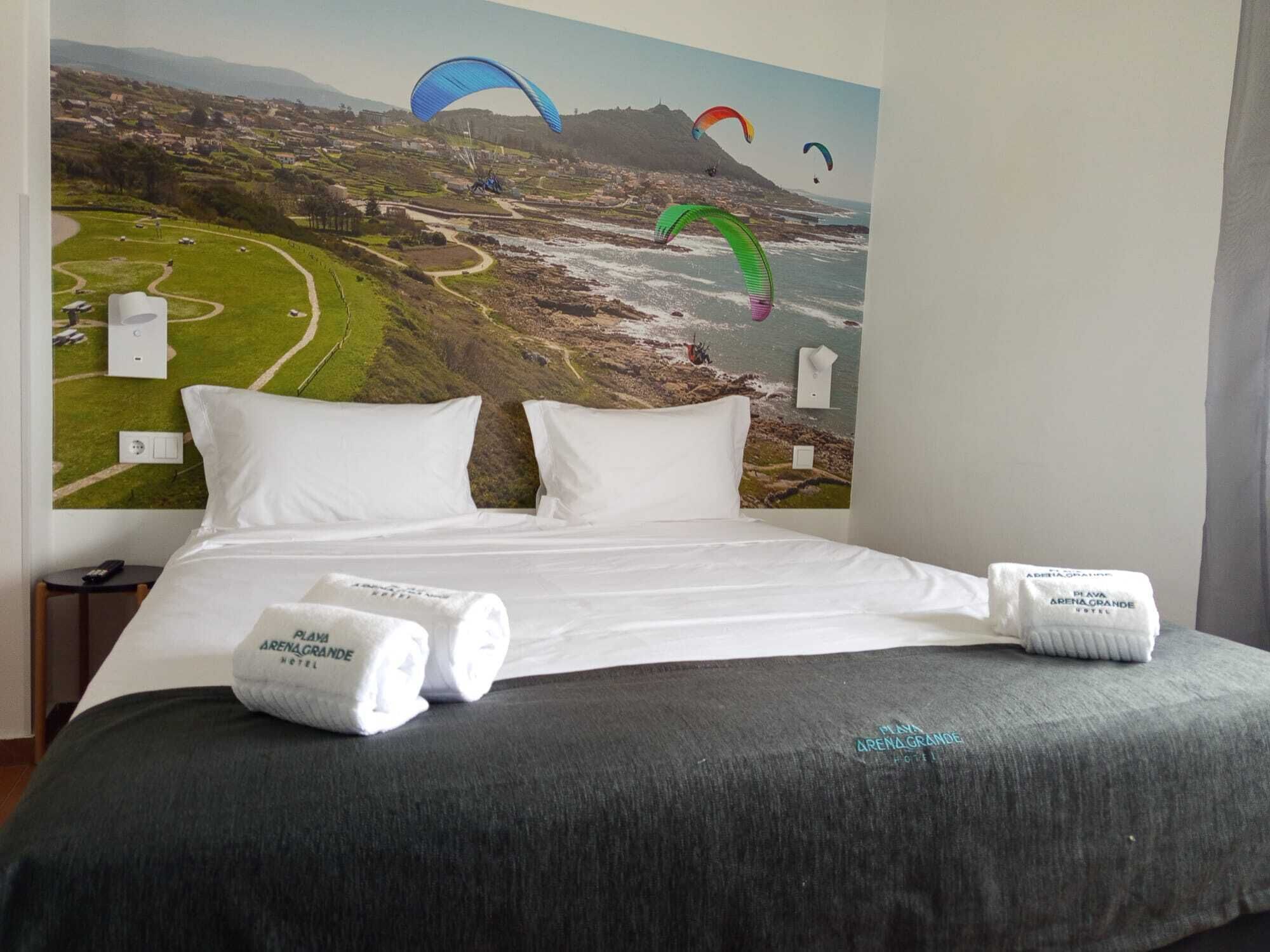 Habitació d'hotel amb un llit, almoines blanques i un mural gran d'un paisatge costaner amb tempestes.