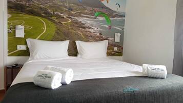 A hotel room with a bed, white pillows, and a large mural of a coastal landscape with kites.