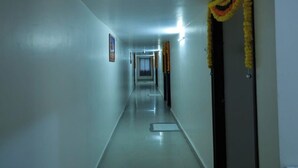 A long, narrow hallway with a polished floor and white walls. There are doors on both sides, one of which is decorated with yellow flowers. - samudra inn (Nalgonda)