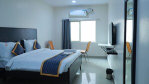 A hotel room with a bed, a desk, a chair, an air conditioning unit, and a television.