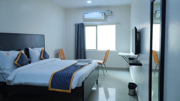 A hotel room with a bed, a desk, a chair, an air conditioning unit, and a television. - samudra inn (Nalgonda)