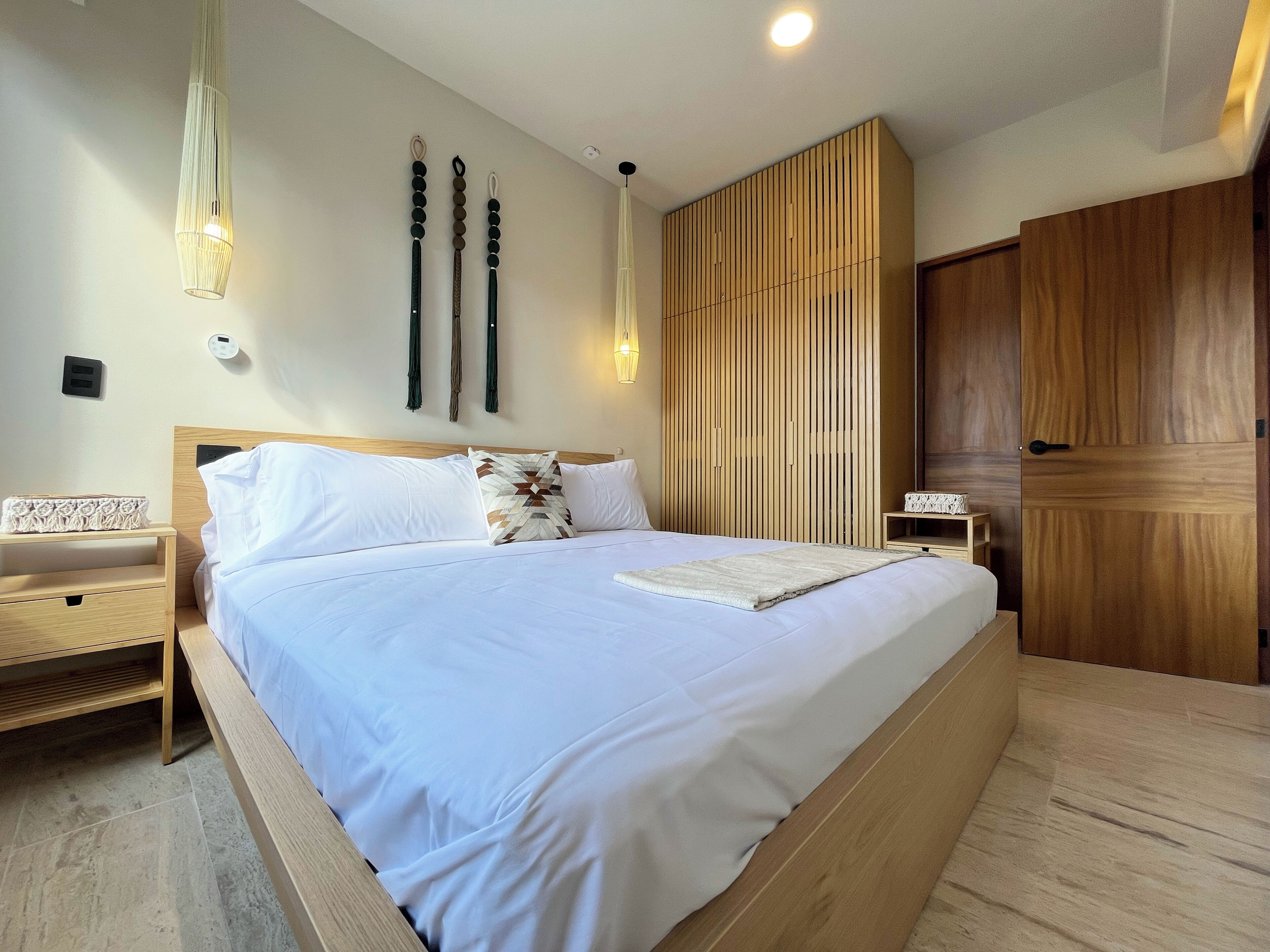 A bedroom with a large bed, wooden headboard, bedside tables, a wardrobe, and a hanging light fixture.